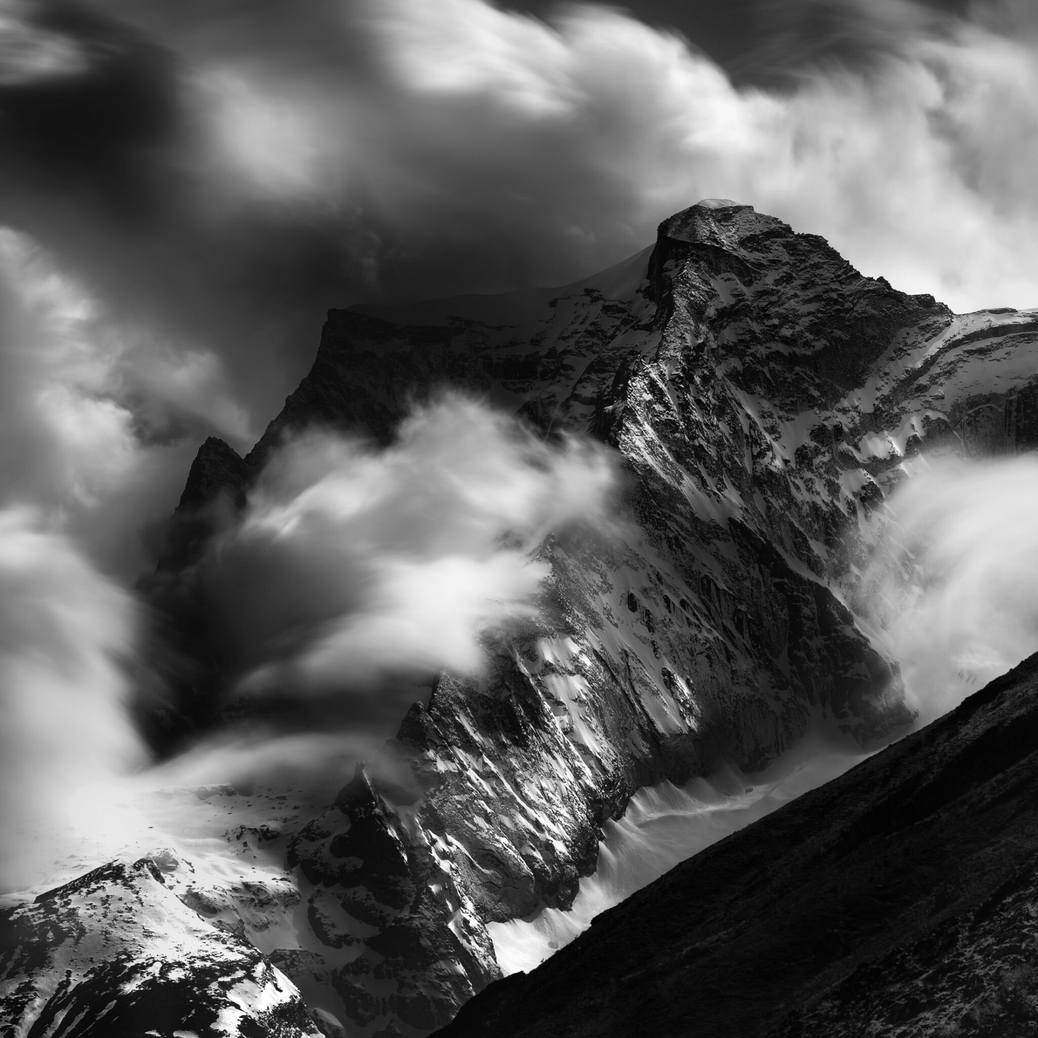 Dramatic black and white fine art photograph of a jagged alpine mountain peak engulfed in swirling storm clouds