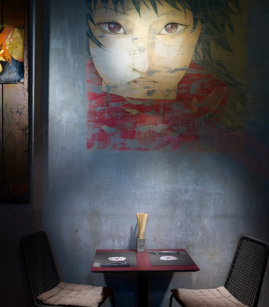 Dark and moody Asian-inspired restaurant interior with a large painted portrait mural and intimate table setting