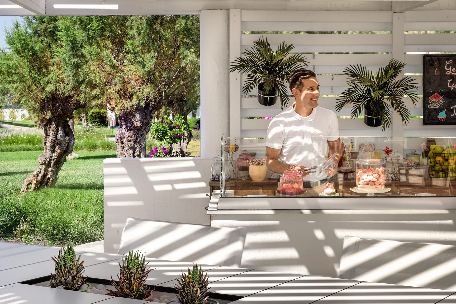 Barkeeper holding a vibrant dessert at a beach bar under the sun