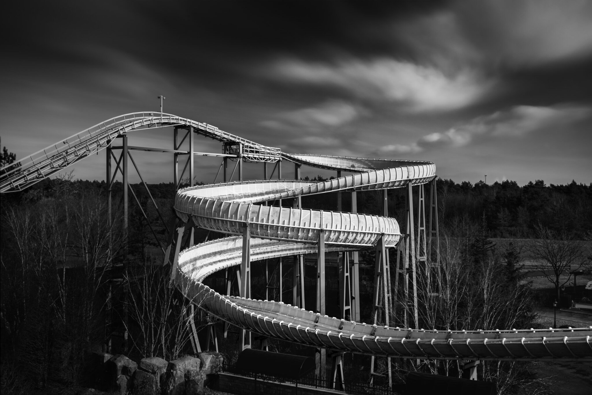 Black and white fine art photograph of a bobsled ride with sweeping curved track structure against a stormy sky