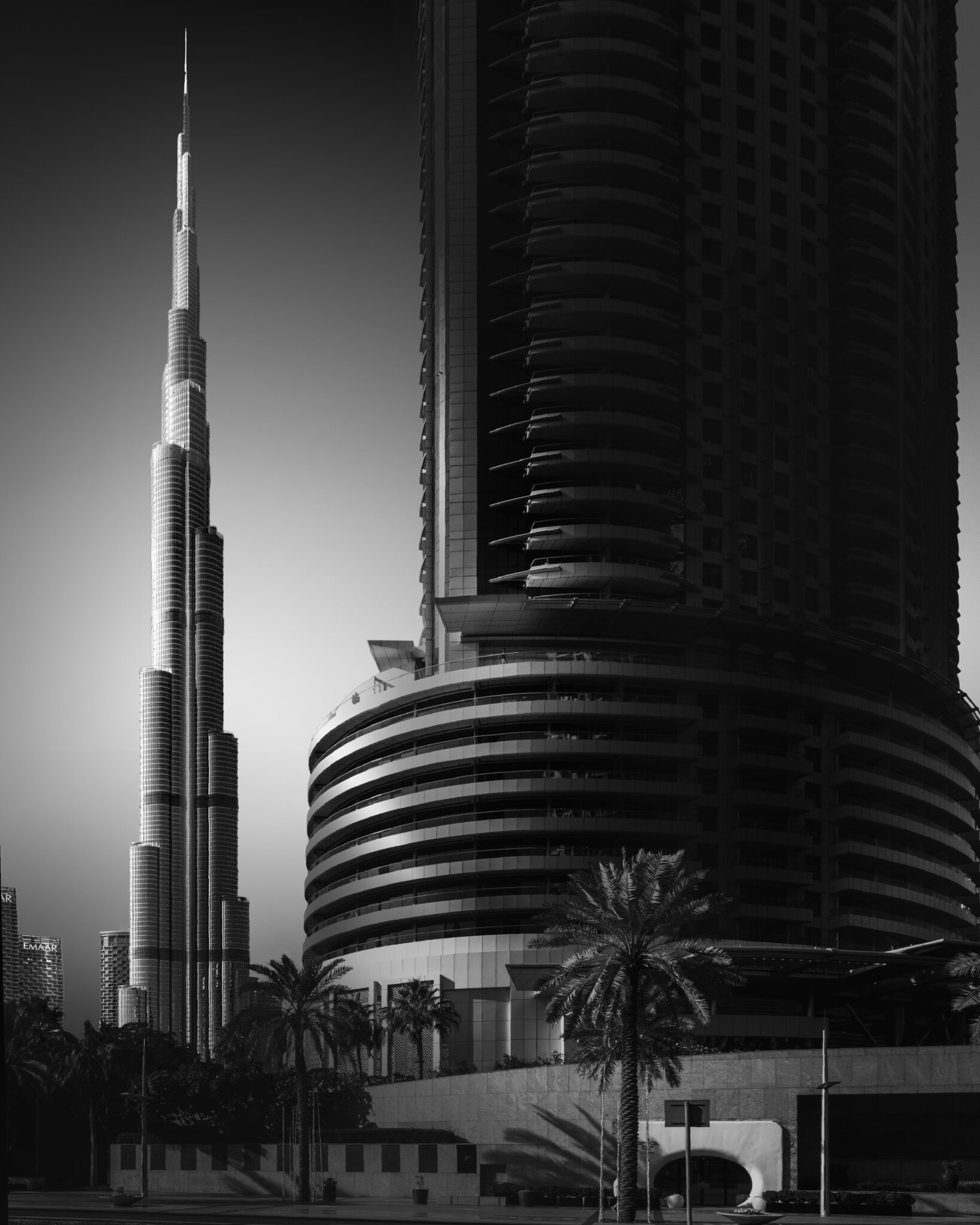 Black and white fine art photograph of the Burj Khalifa towering above the Dubai skyline with palm trees and historic buildings
