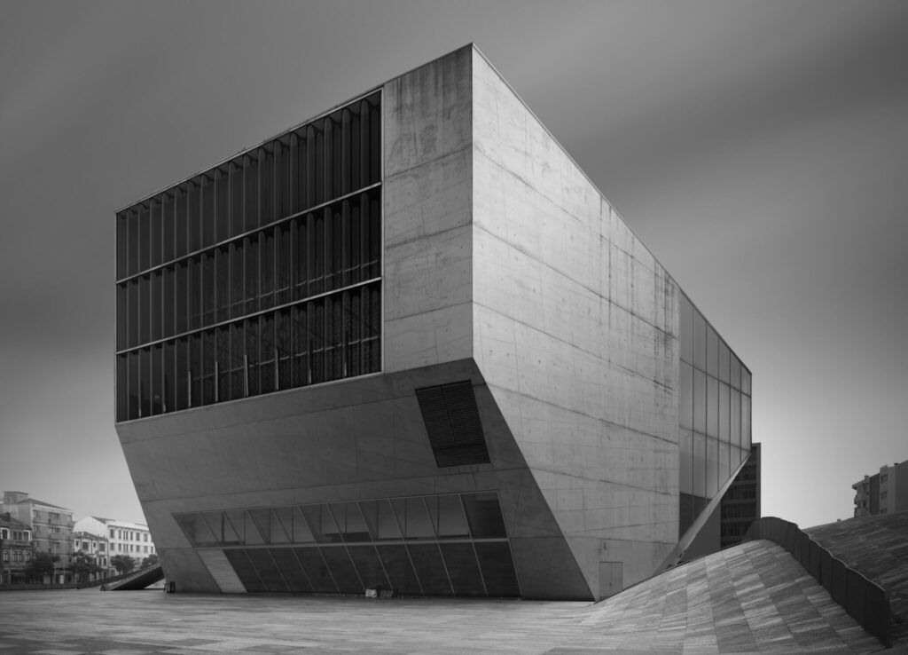 Black and white fine art photograph of a bold brutalist concert hall with a cantilevered concrete cube beside a waterfront