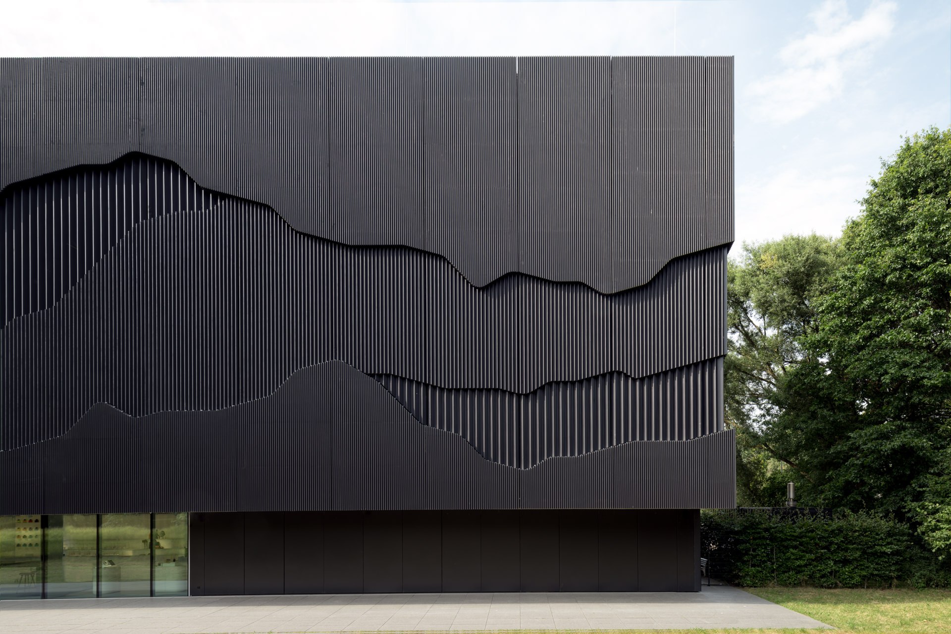 Fine art architectural detail of a dark corrugated metal building facade with organic wave-cut relief shapes