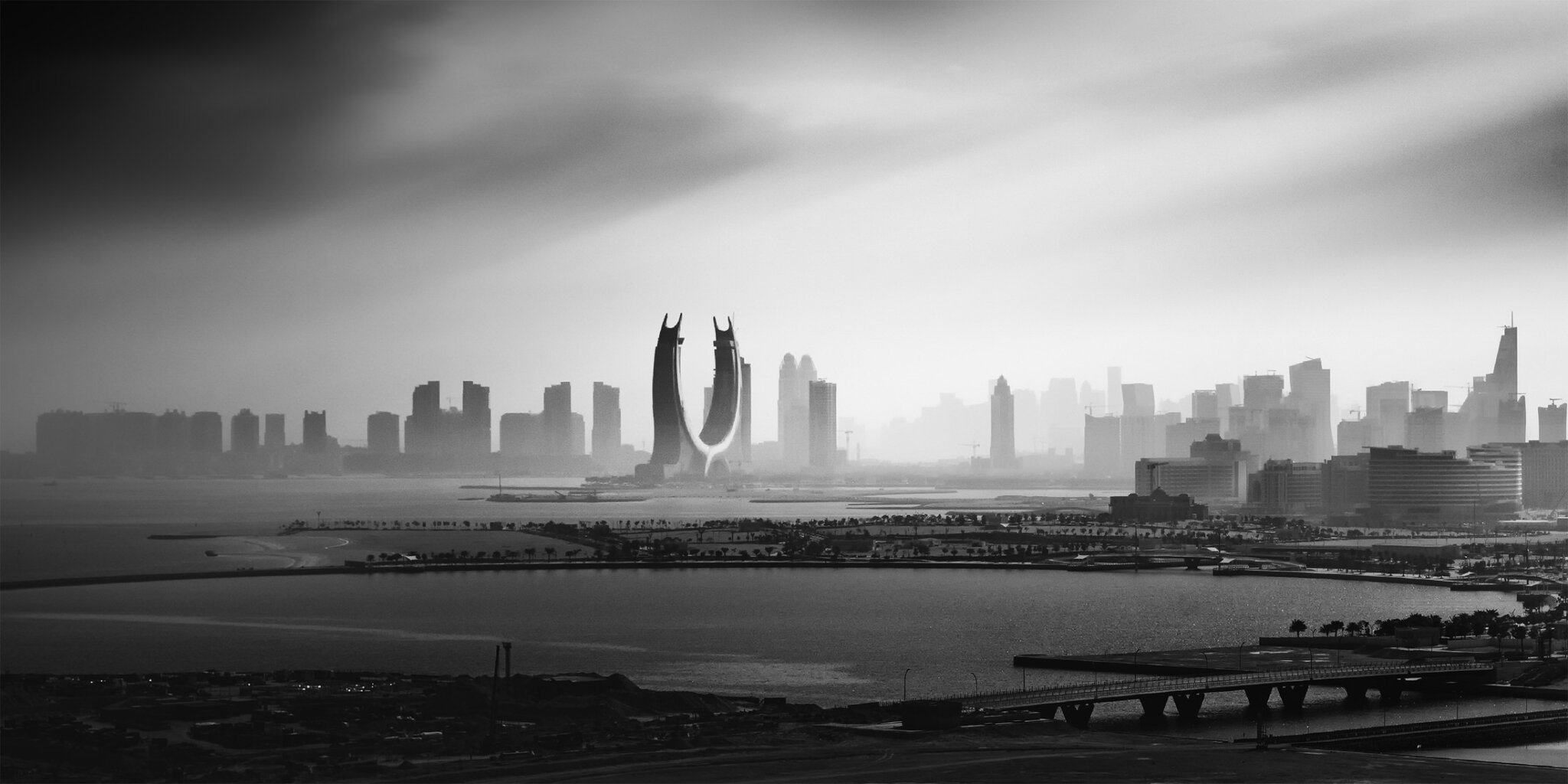 dramatic black and white image of a backlit city skyline by the ocean
