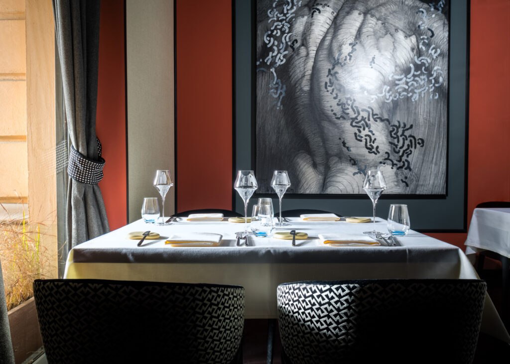 Intimate fine dining setting with a single white linen table, dramatic framed artwork, and carefully arranged glassware