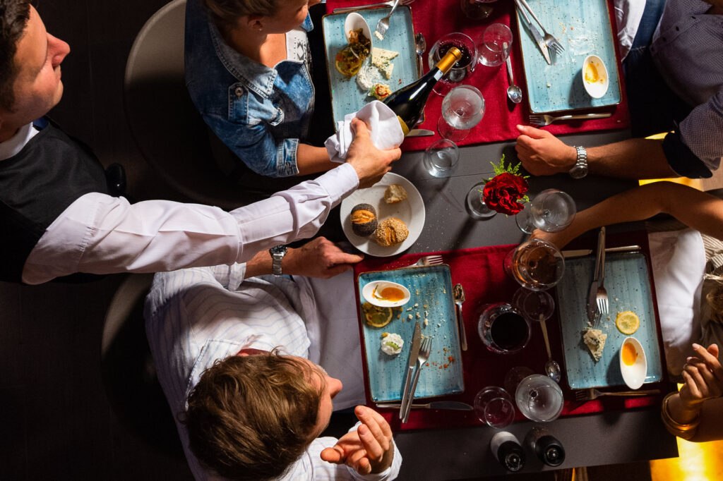 Overhead shot of guests at a fine dining wine terrace with hands reaching across shared dishes and colorful food presentation