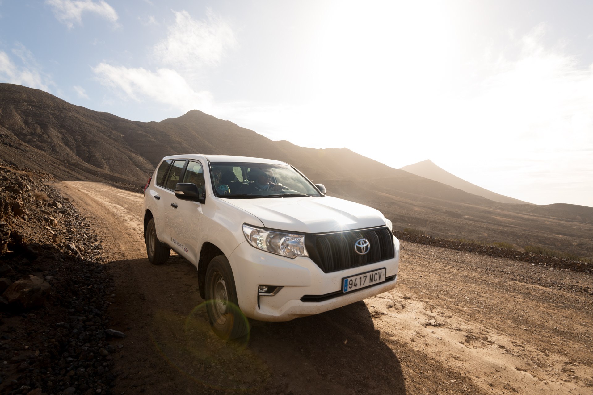 White 4x4 SUV parked on a dramatic volcanic desert road at sunset in Fuerteventura — adventure travel photography