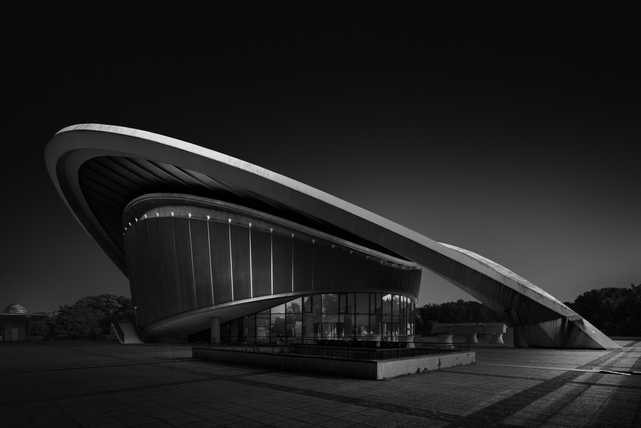 Black and white fine art photograph of a futuristic oval pavilion building with curved roofline illuminated at night
