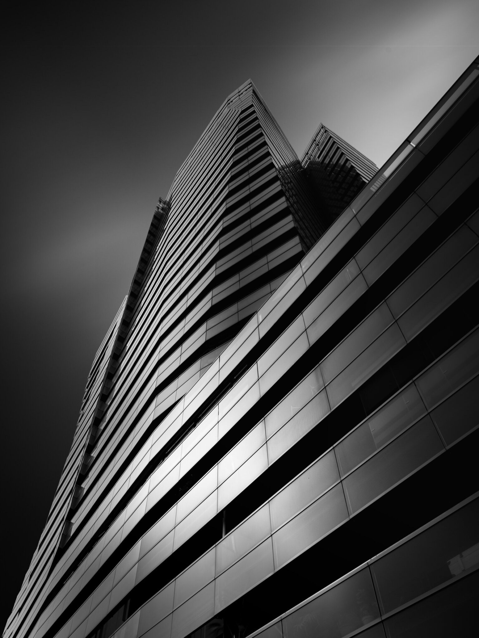 Low-angle black and white fine art photograph of a glass curtain-wall building facade with bold diagonal geometry
