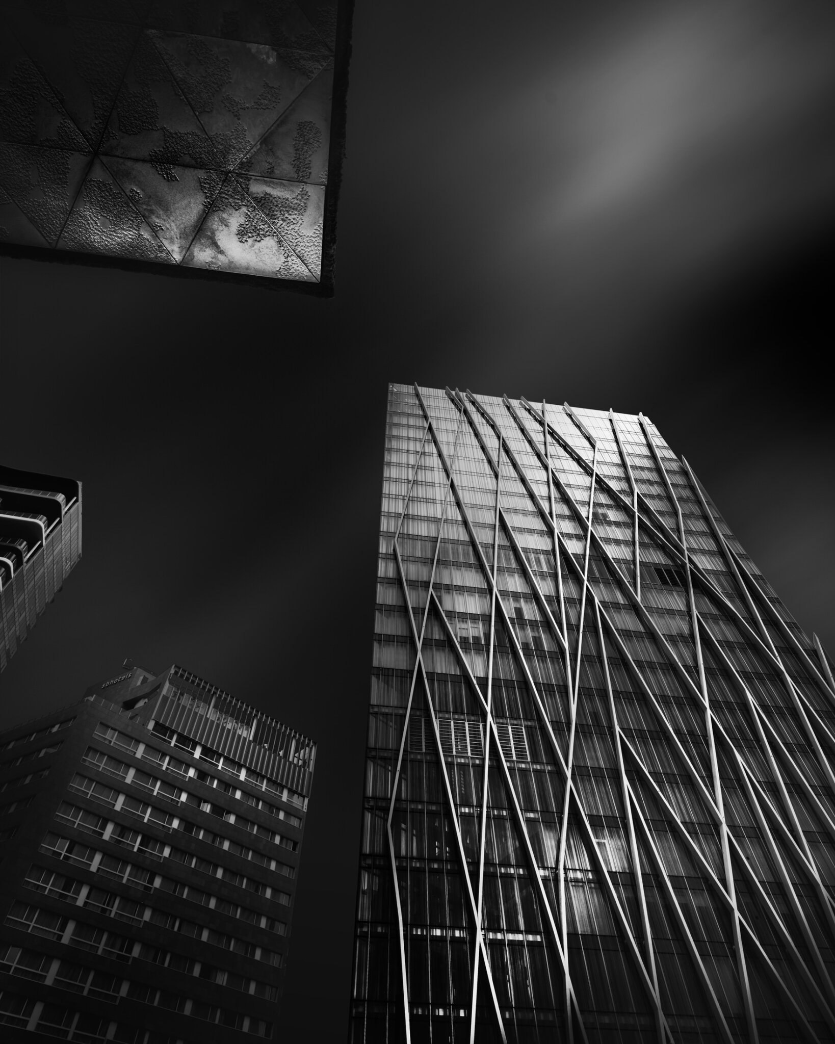 Low-angle black and white fine art photograph of intersecting glass building facades with bold diagonal geometry