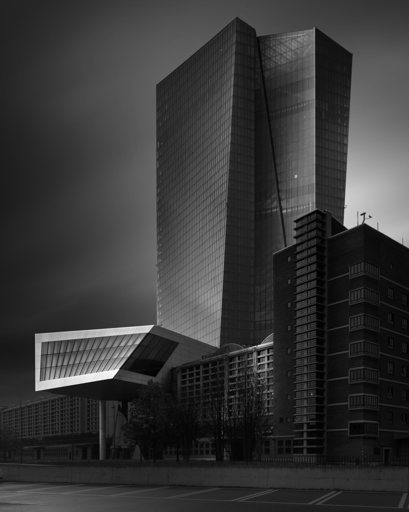 Black and white fine art photograph of a glass skyscraper complex with bold cantilevered elements on an urban street