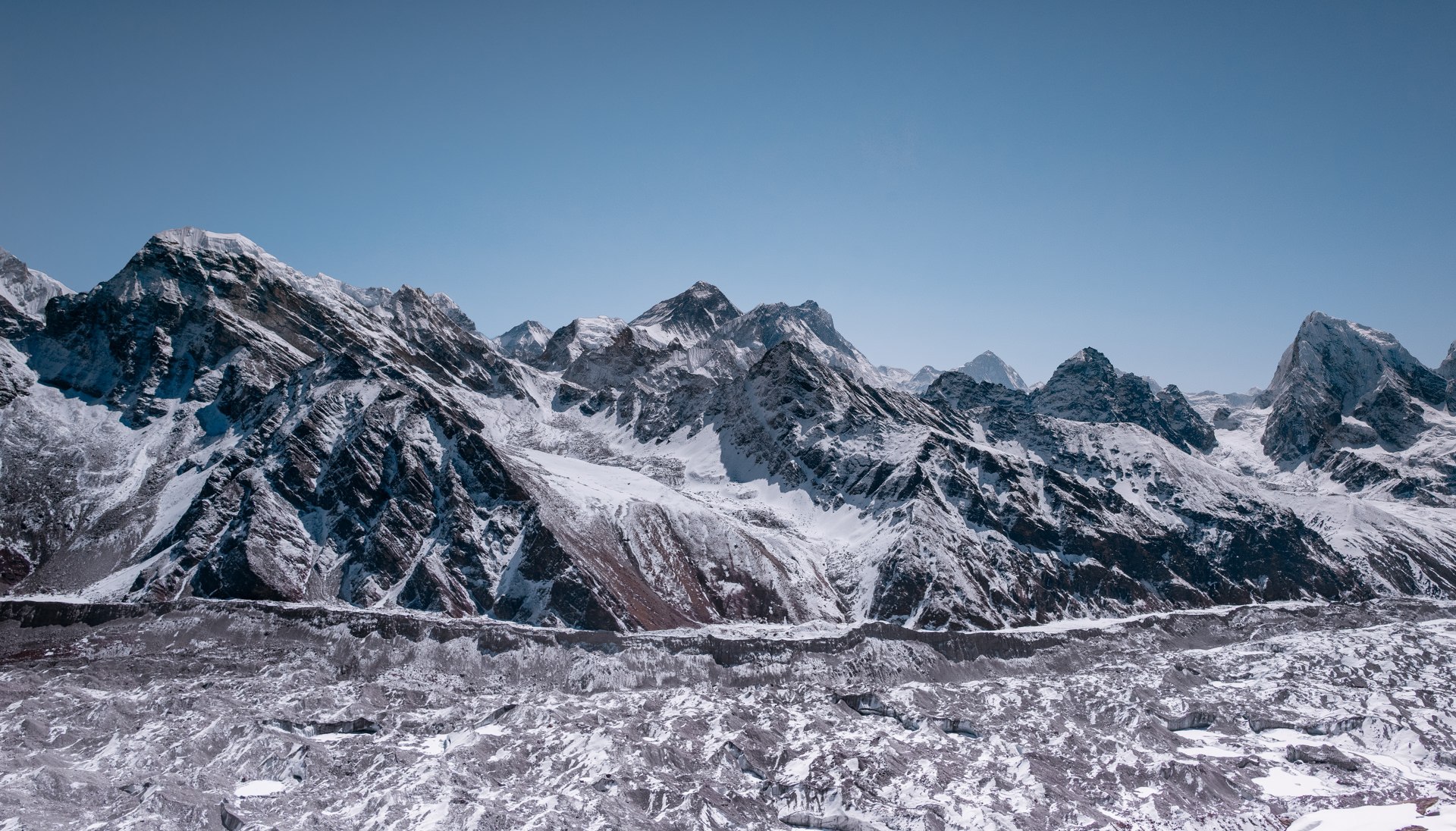 Wide-angle panorama of snow-capped Himalayan peaks and a glacier under a bright blue sky