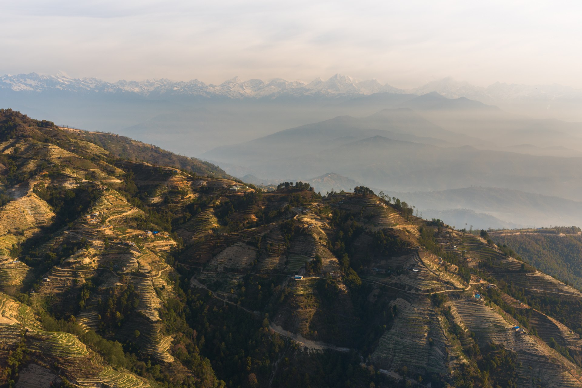 Aerial landscape of dramatic Himalayan mountain ridges with terraced hillsides bathed in golden afternoon light