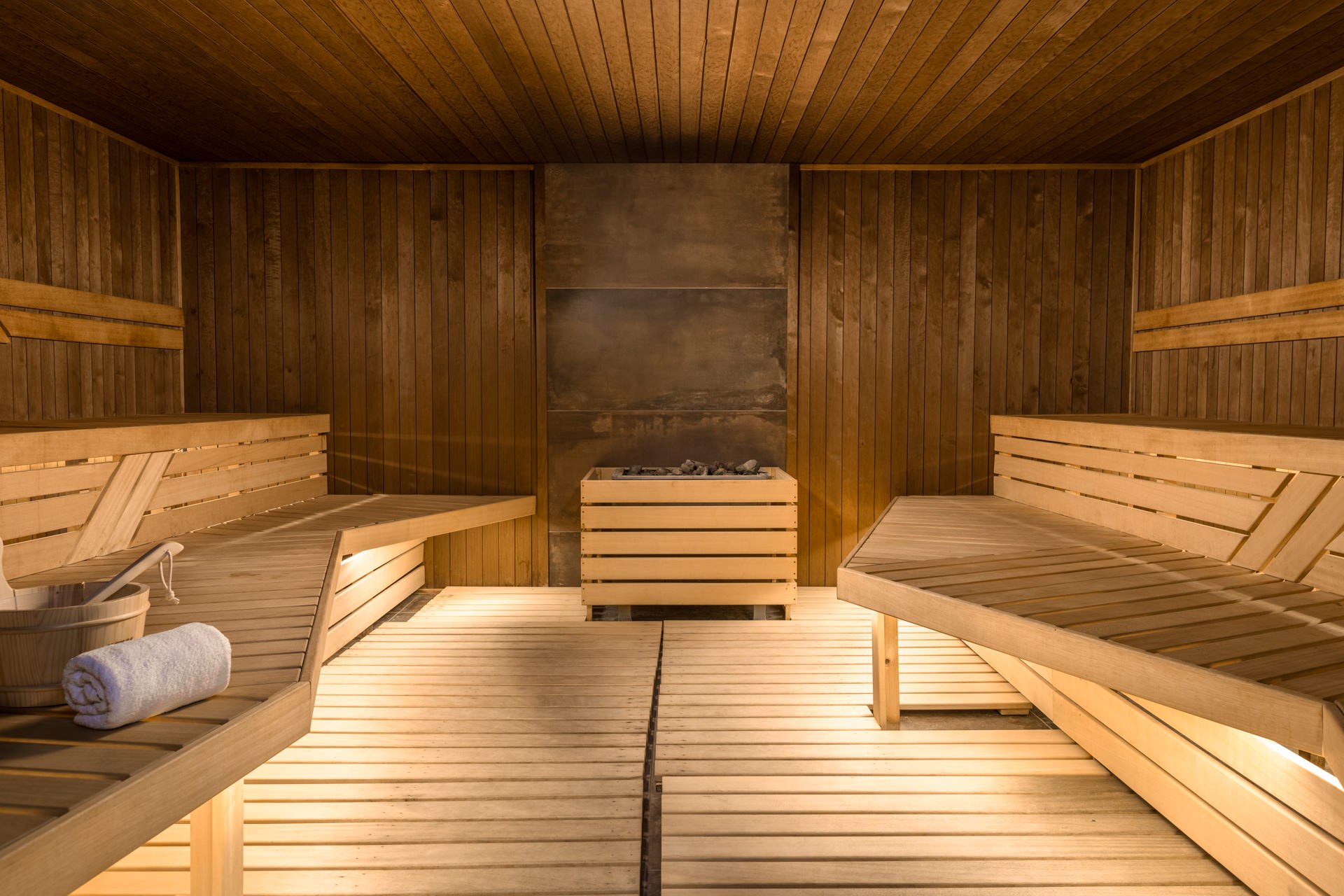 Warm hotel sauna interior with cedar wood walls, tiered benches, and a rolled towel — luxury spa photography