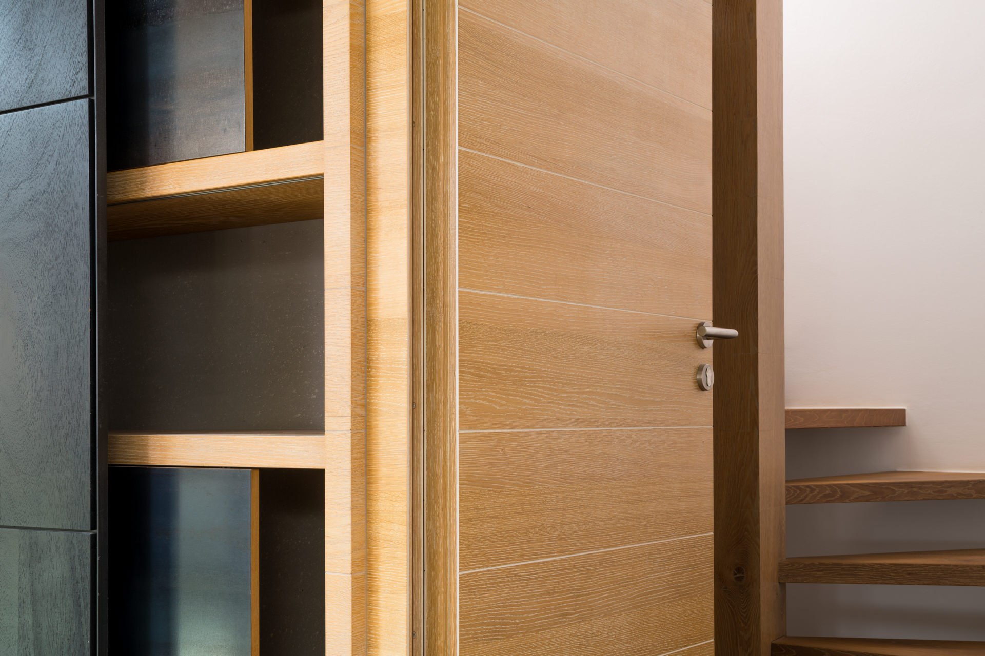 Architectural interior with custom warm oak wardrobe door, built-in shelving, and an adjacent open staircase