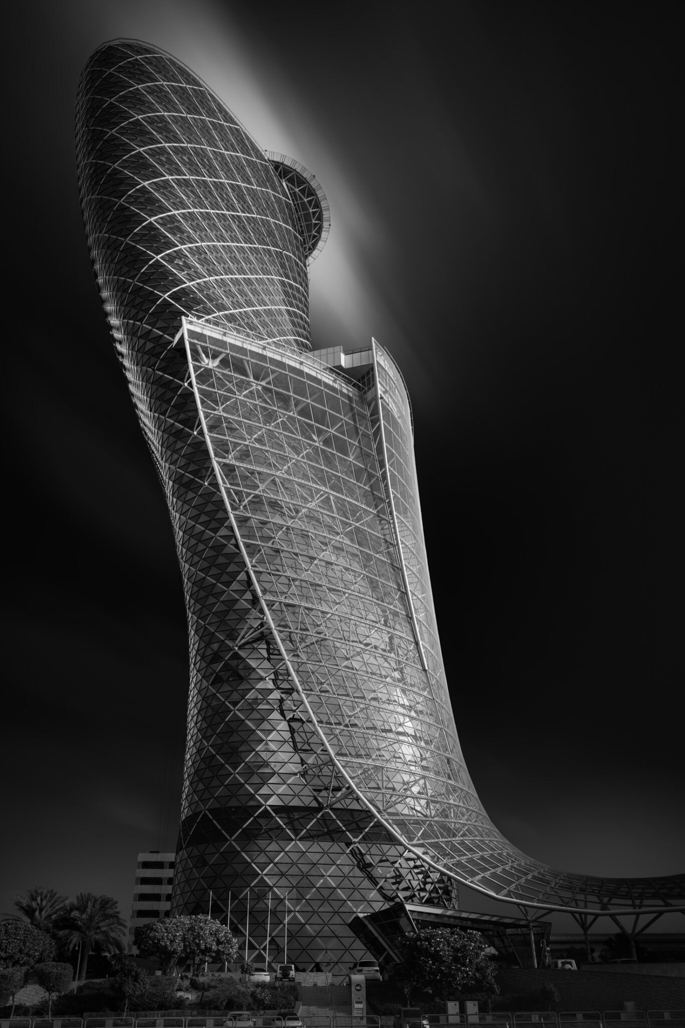 Black and white fine art photograph of a dramatically leaning lattice-facade tower housing the andaz capitalgate hotel in abu dhabi