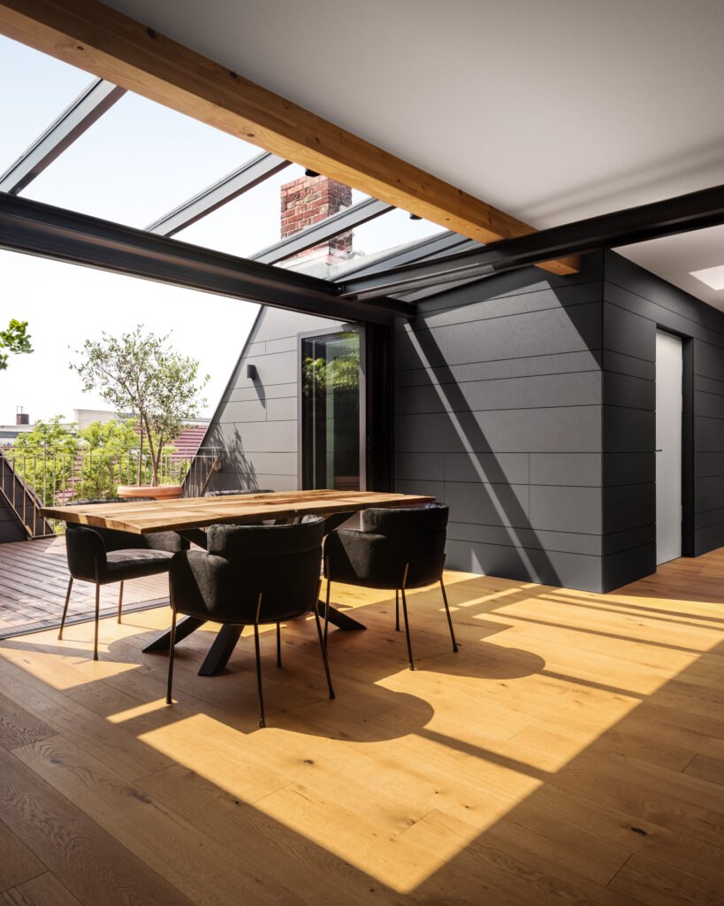 Sun-drenched loft living and dining area with large skylights, wooden flooring, and a terrace opening
