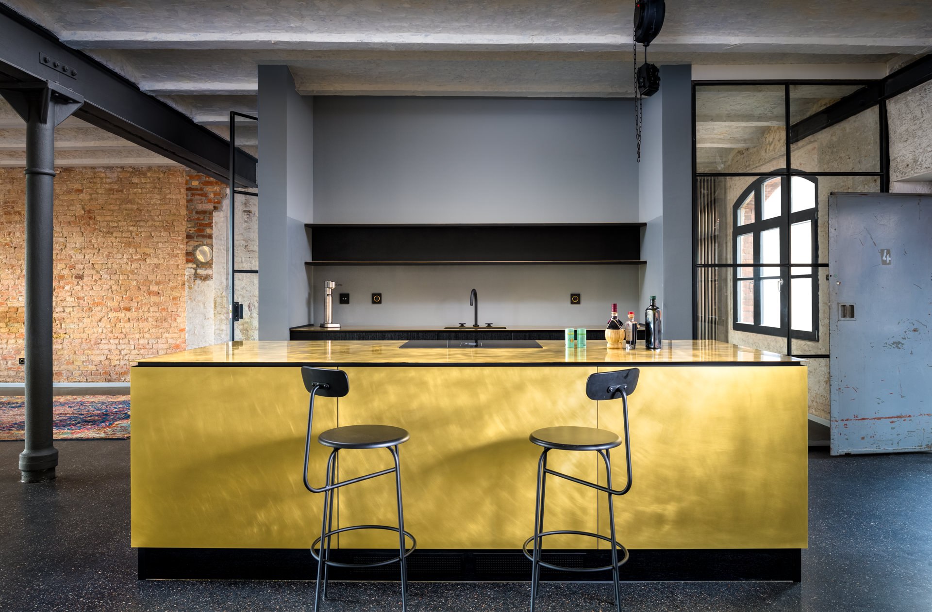 Spacious industrial loft with a bold gold-clad kitchen island, bar stools, and exposed steel ceiling beams