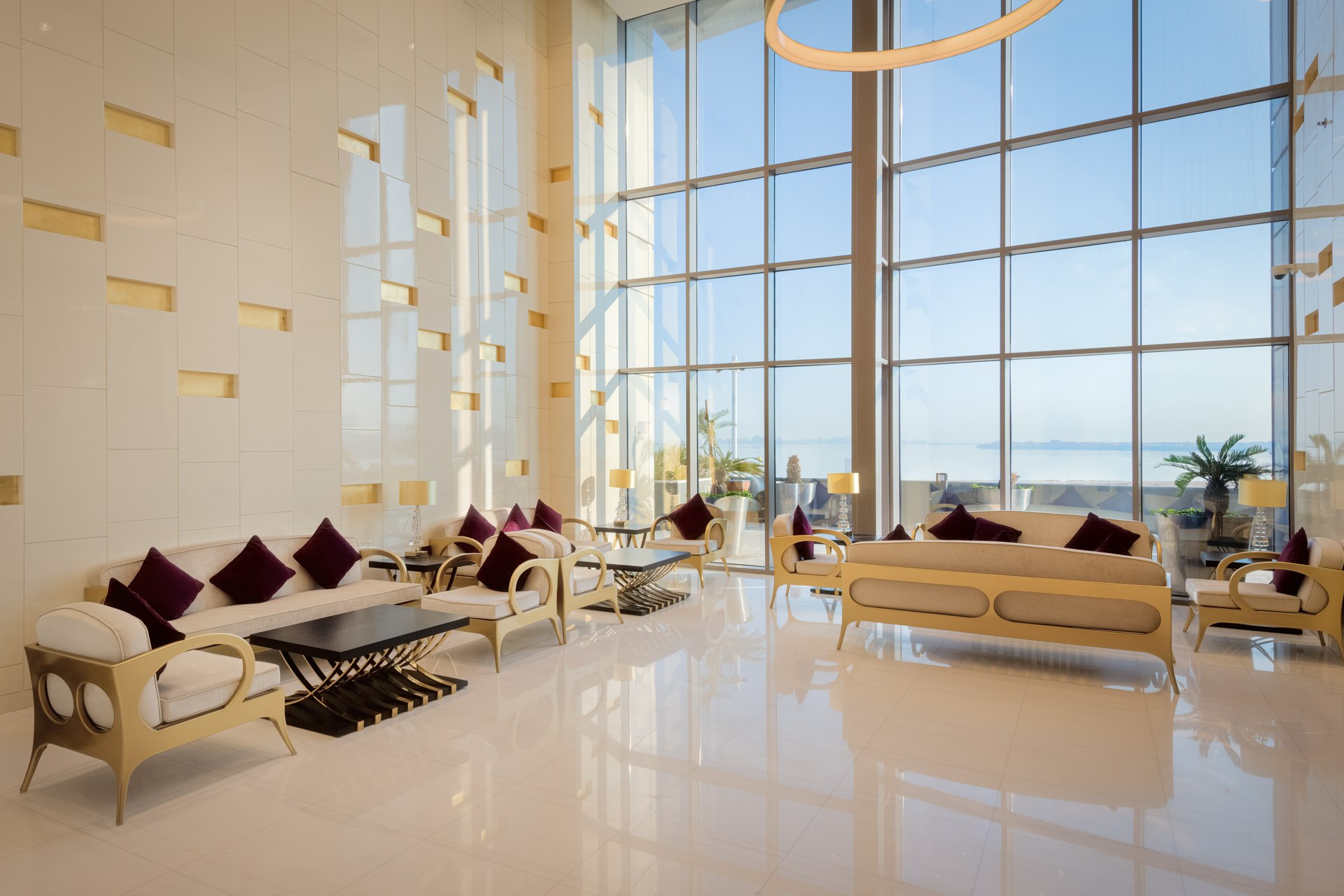 Spacious luxury hotel lobby with floor-to-ceiling windows, marble floors, and contemporary lounge seating overlooking the sea