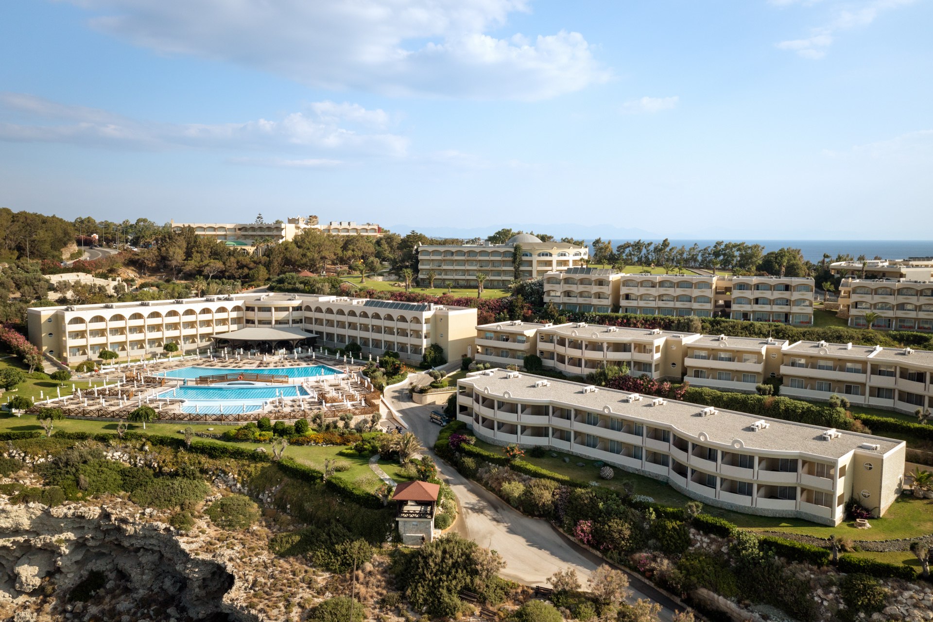 Aerial view of a Mediterranean resort with a large swimming pool, lush garden landscaping, and hotel wings