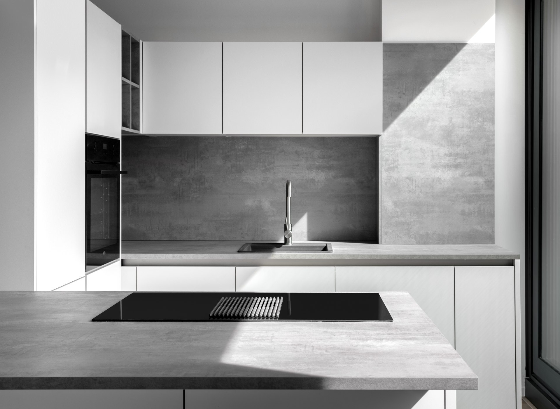 Clean minimalist kitchen with white high-gloss cabinets, dark induction hob, and flush-mounted sink