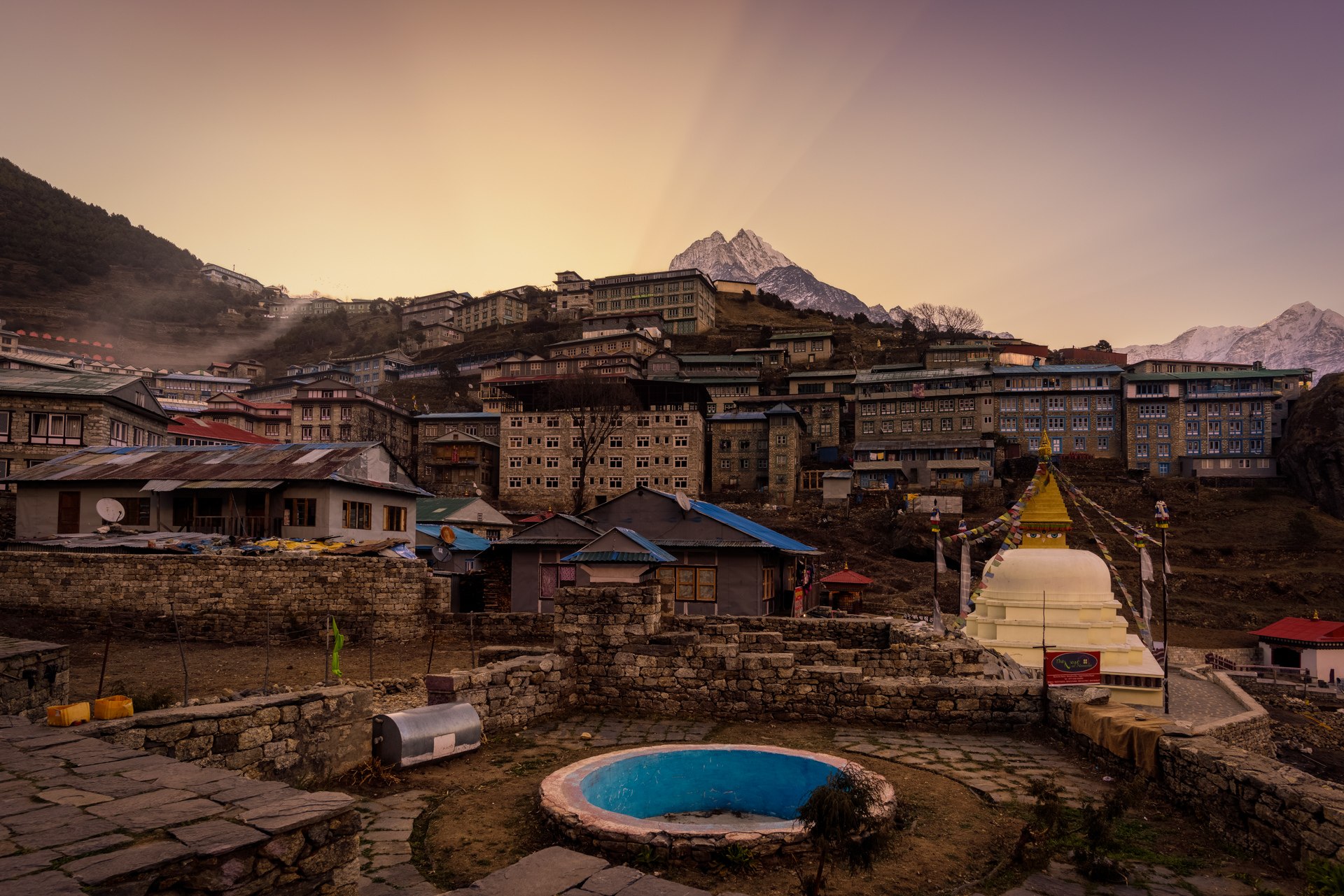 Overhead view of a traditional Himalayan village with a white Buddhist stupa, rooftops, and a dramatic golden sky