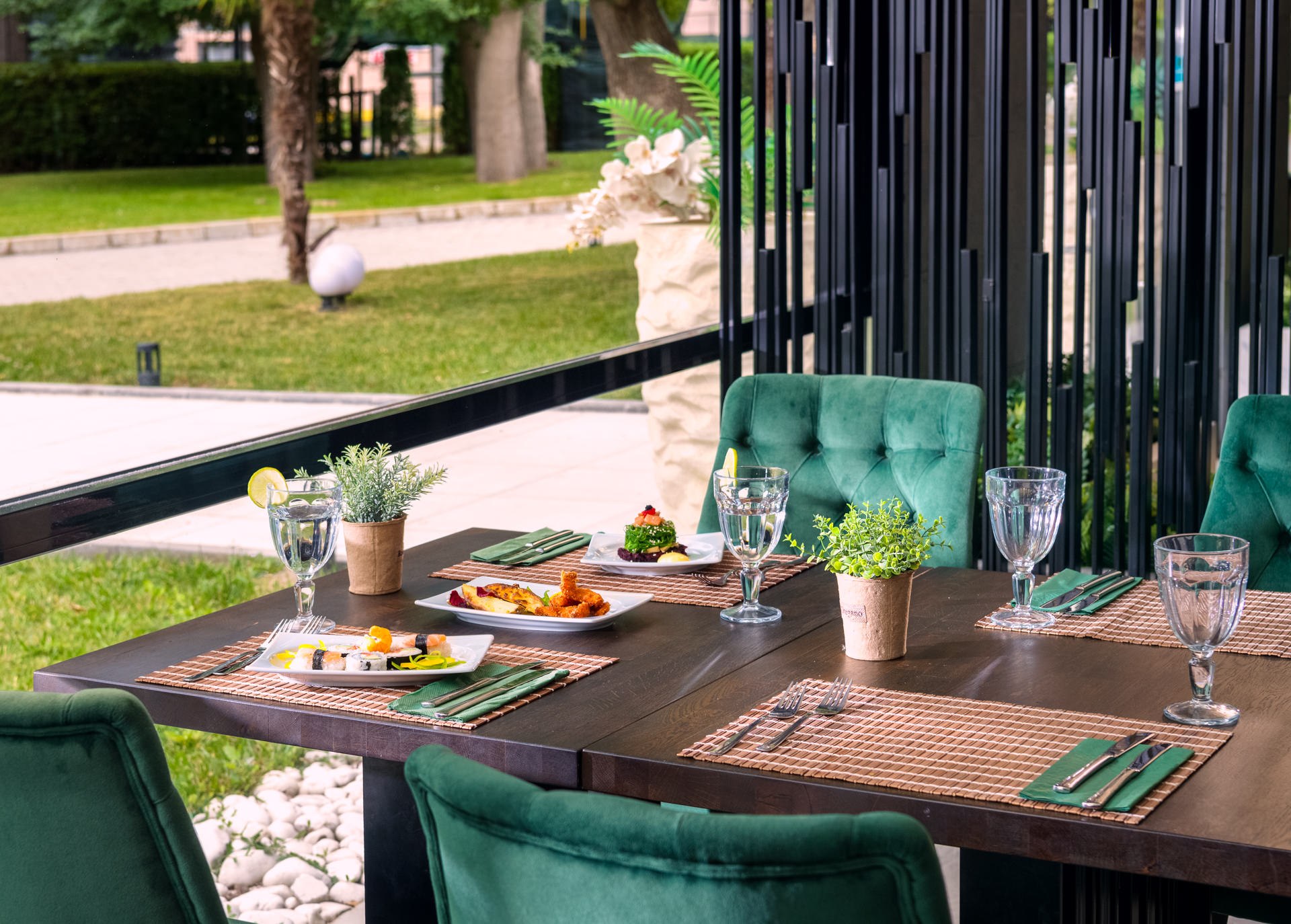 Outdoor restaurant table with green velvet chairs set in a garden with drinks and food — al fresco dining photography