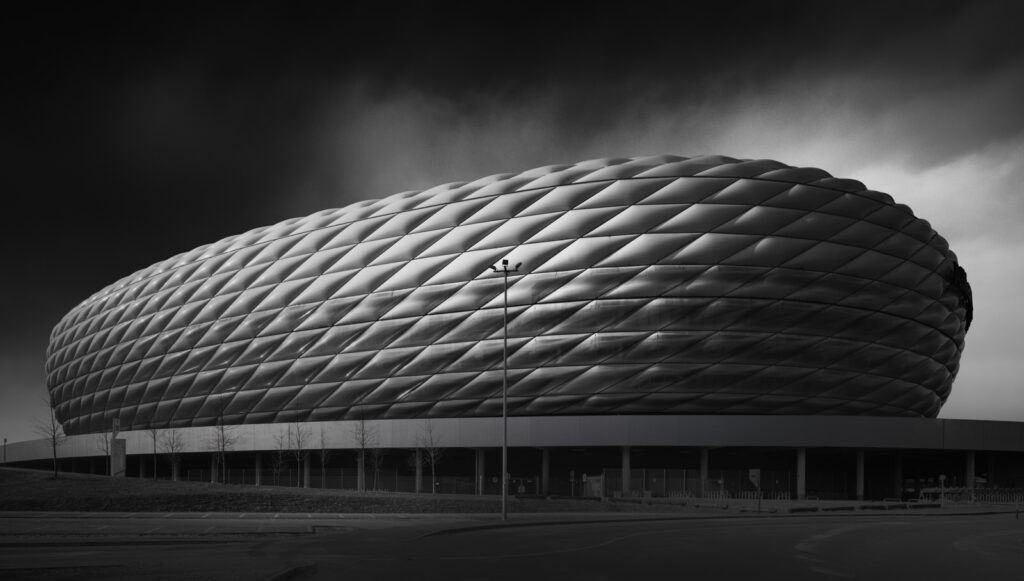 Black and white fine art photograph of an iconic oval stadium with a diamond-pattern facade under a dark stormy sky