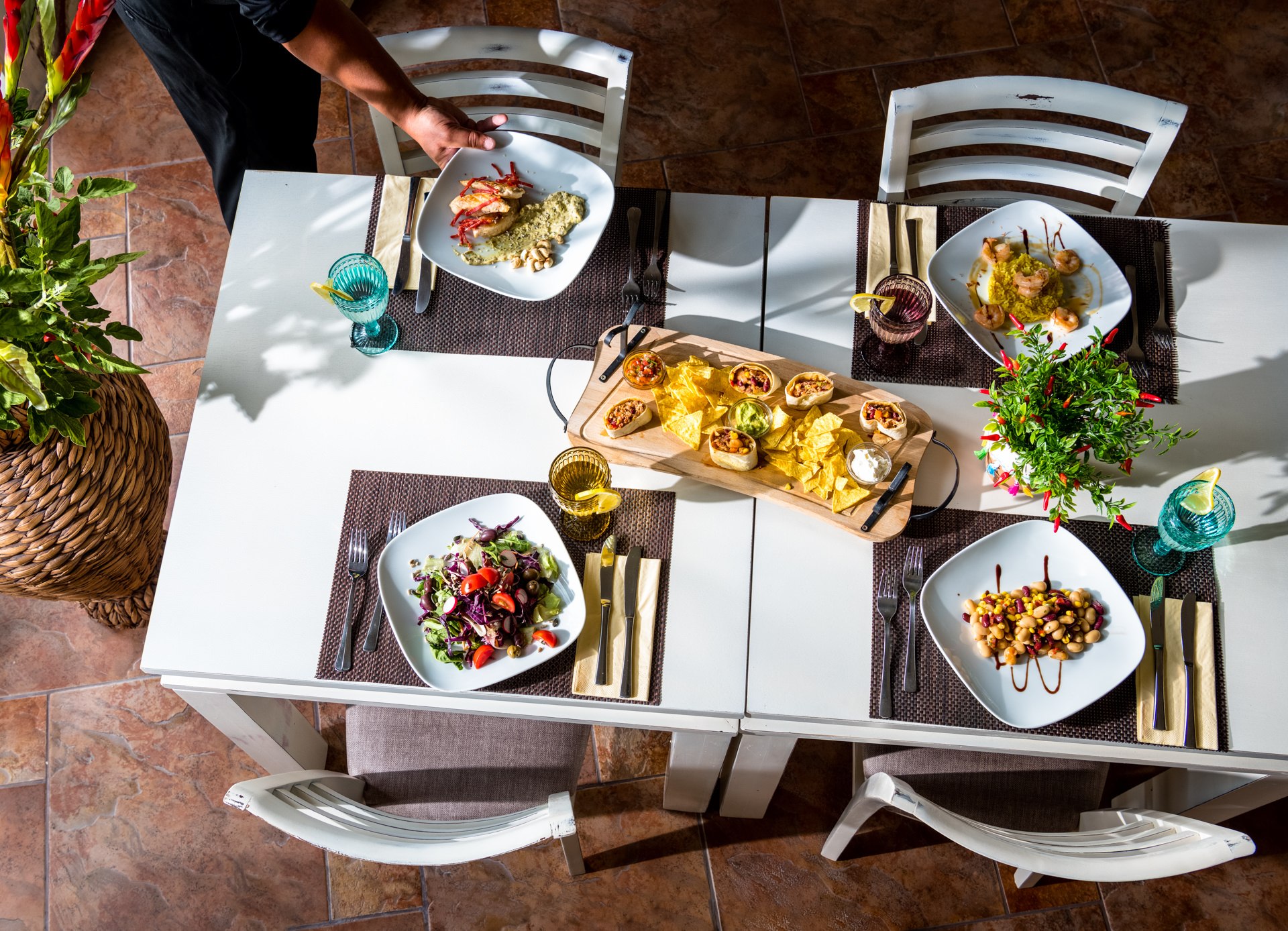 Top-down view of a restaurant table with multiple sharing plates, colorful dishes, and hands reaching across