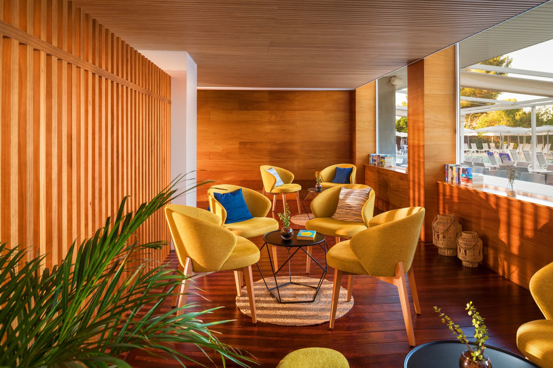 Resort lounge bar with warm wooden ceiling, yellow velvet armchairs, and views of the beach — hospitality interior photography