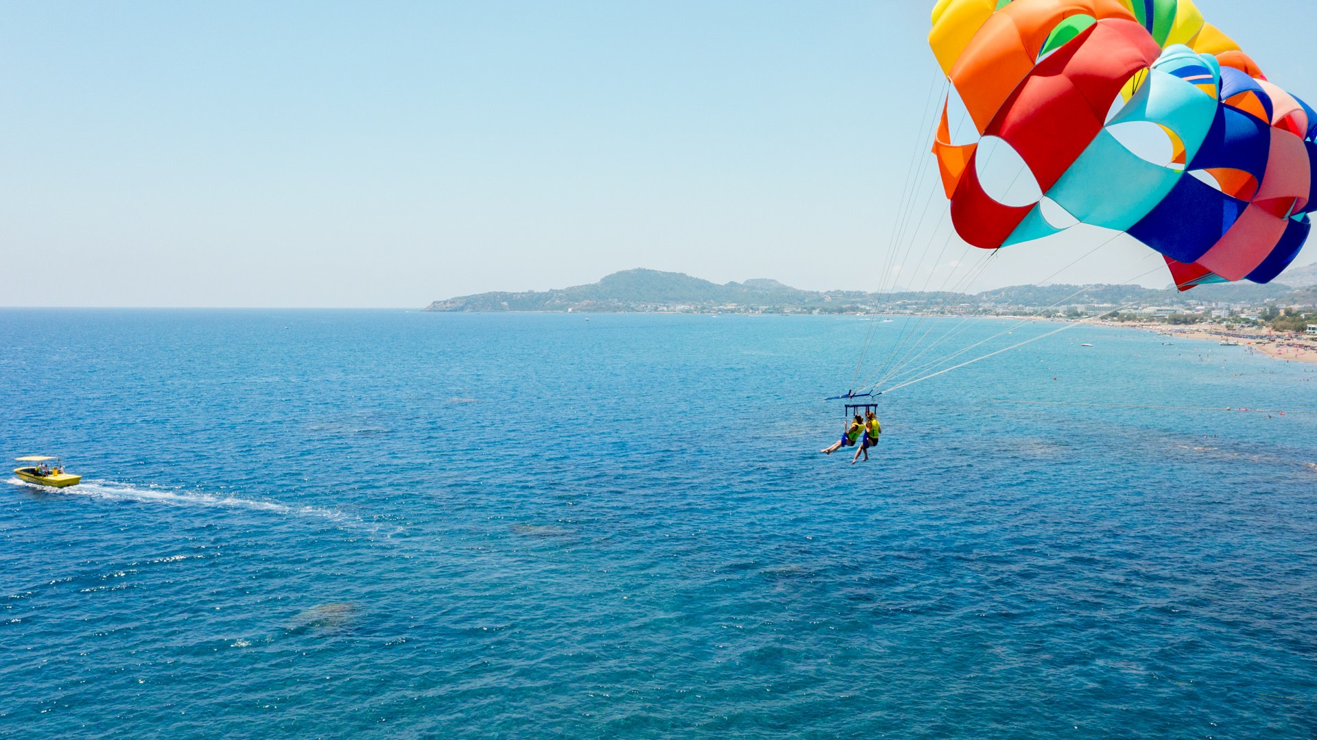 Colorful parasail flying over a deep blue Mediterranean sea with a speedboat below — luxury resort water sports