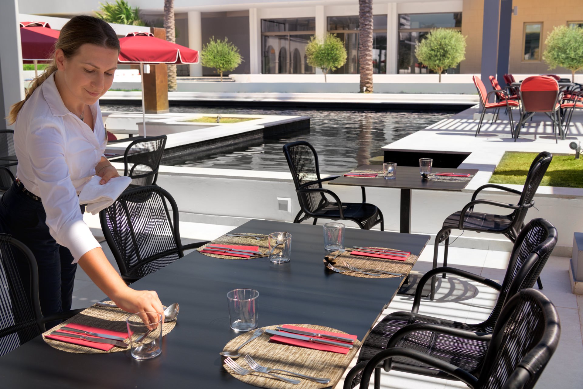Waiter in white shirt carefully setting an outdoor restaurant table at a luxury Mediterranean resort