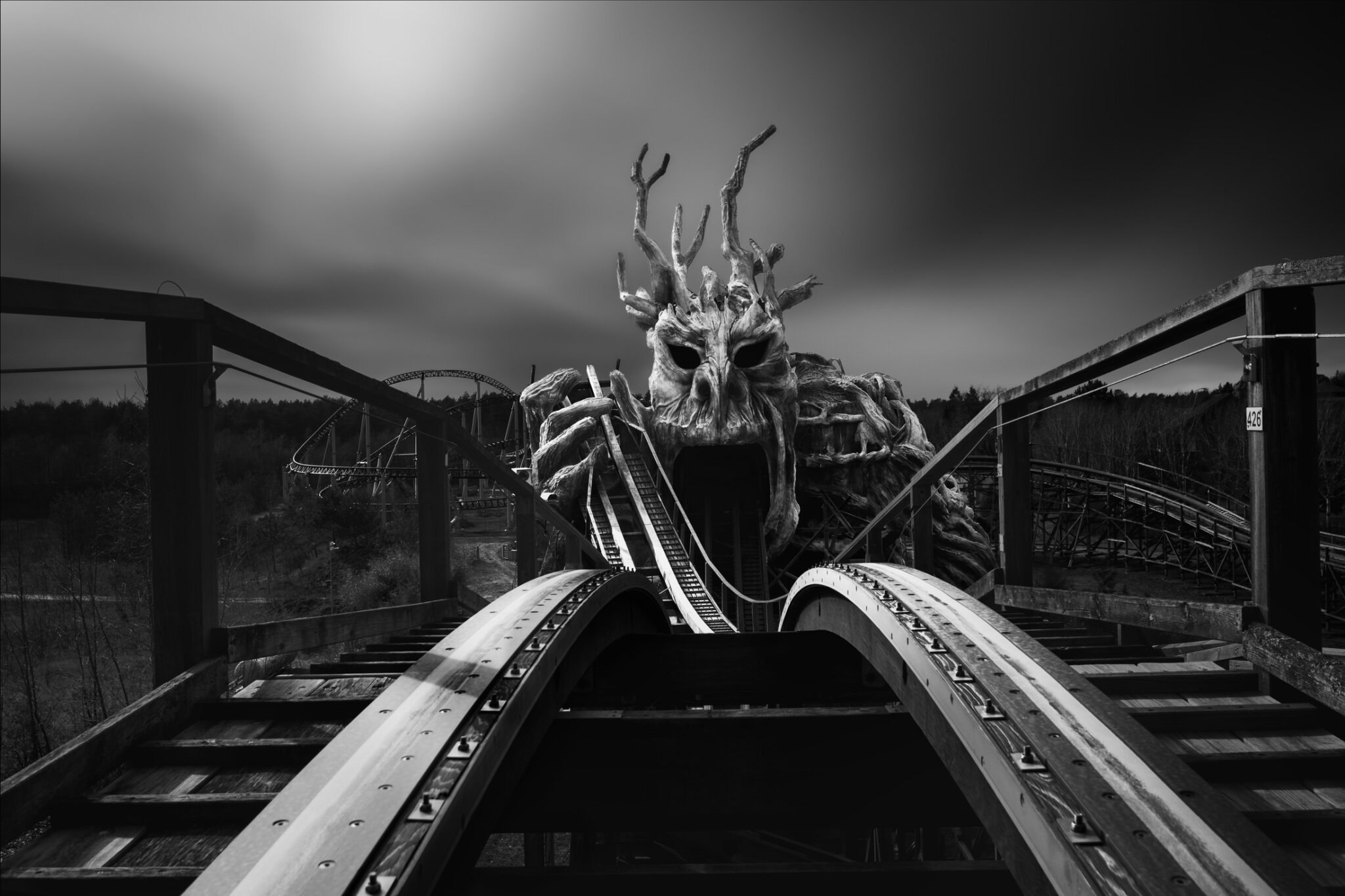 Black and white fine art close-up from a rollercoaster track approaching a large monster figure sculpture