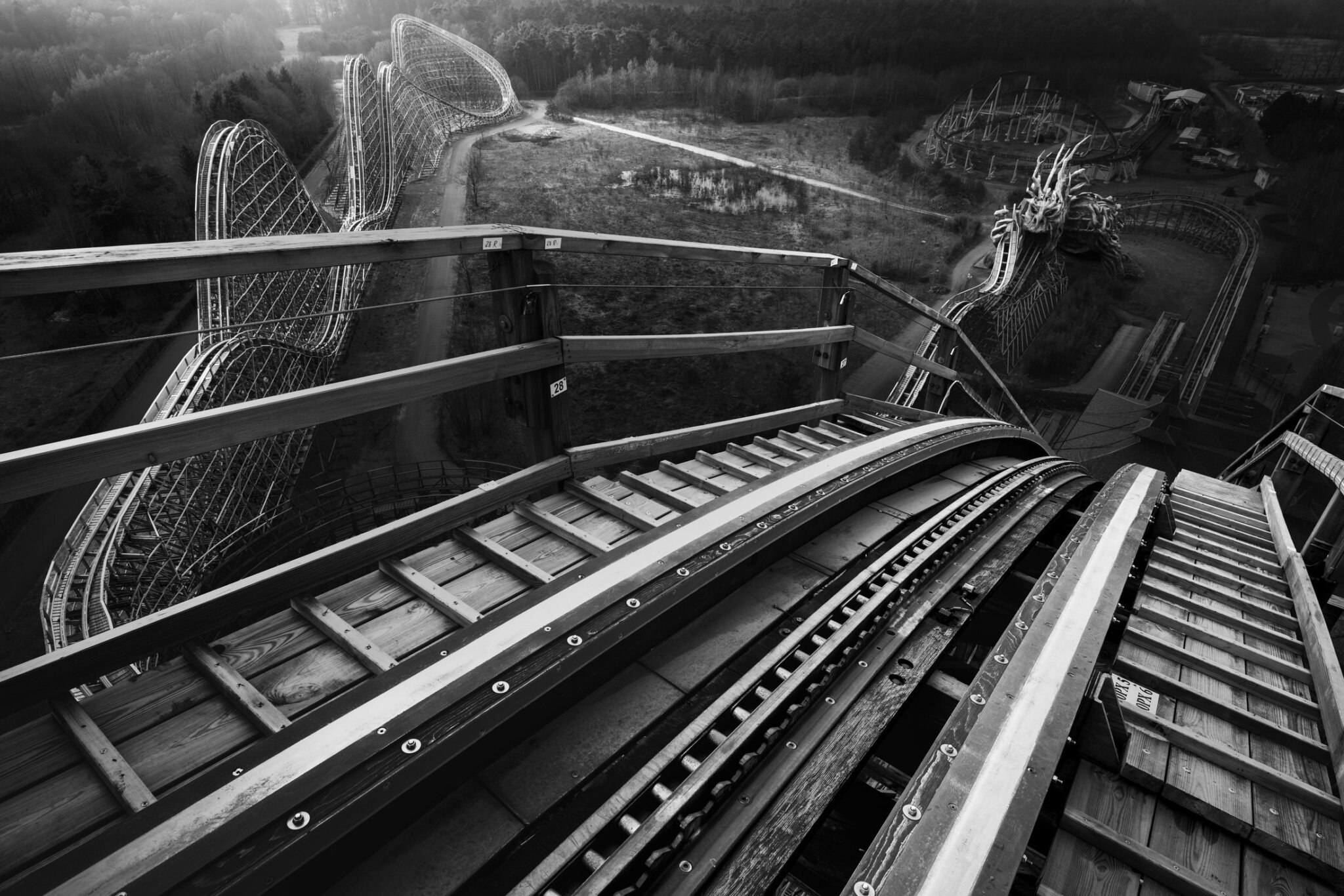 Black and white fine art POV photograph from a wooden rollercoaster with a menacing monster sculpture in the foreground