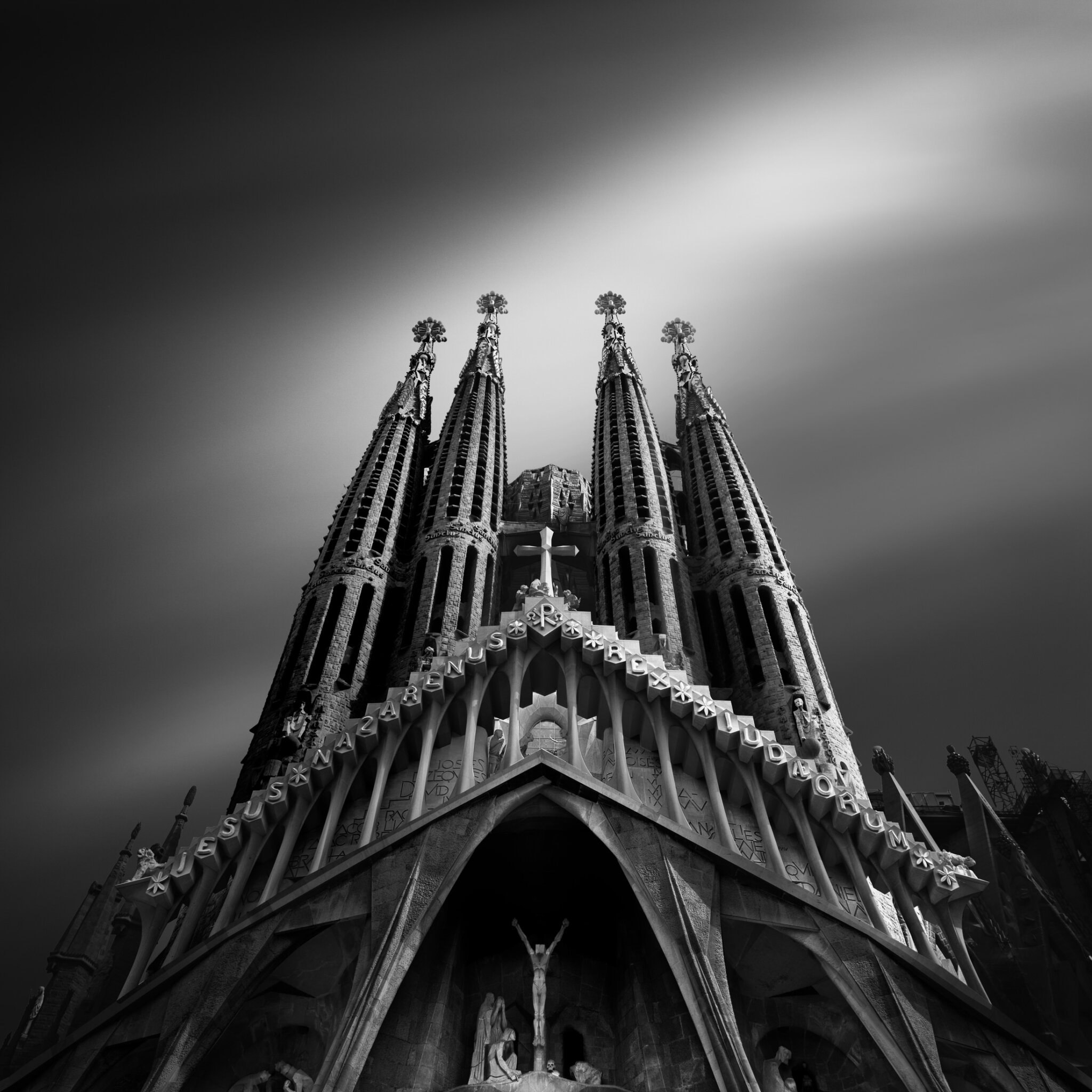 Long exposure black and white fine art photograph looking up at the Gothic spires of the Sagrada Família with a glowing sky