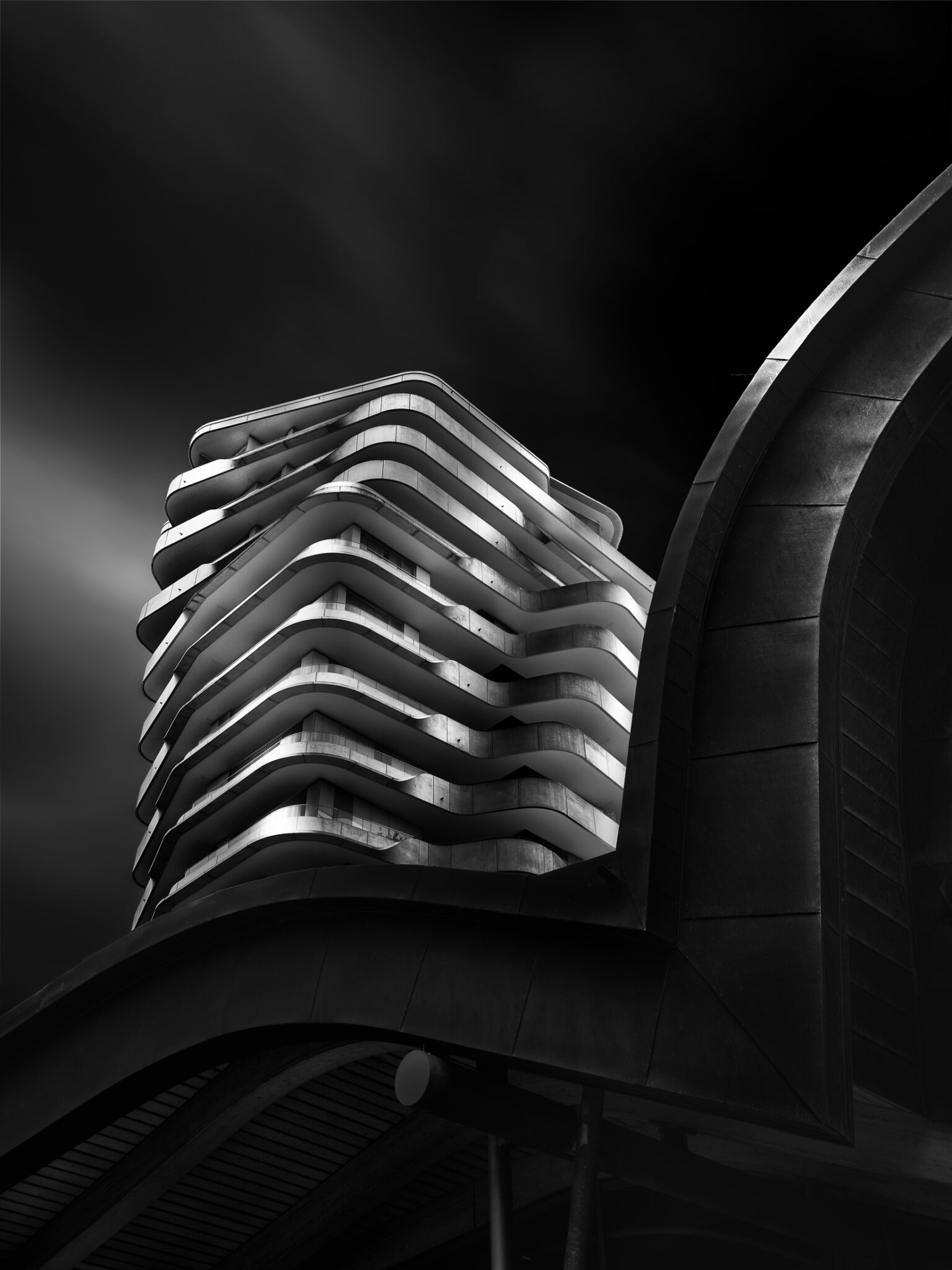 Black and white fine art photograph of a contemporary tower with dramatically stacked curved balconies against a dark sky