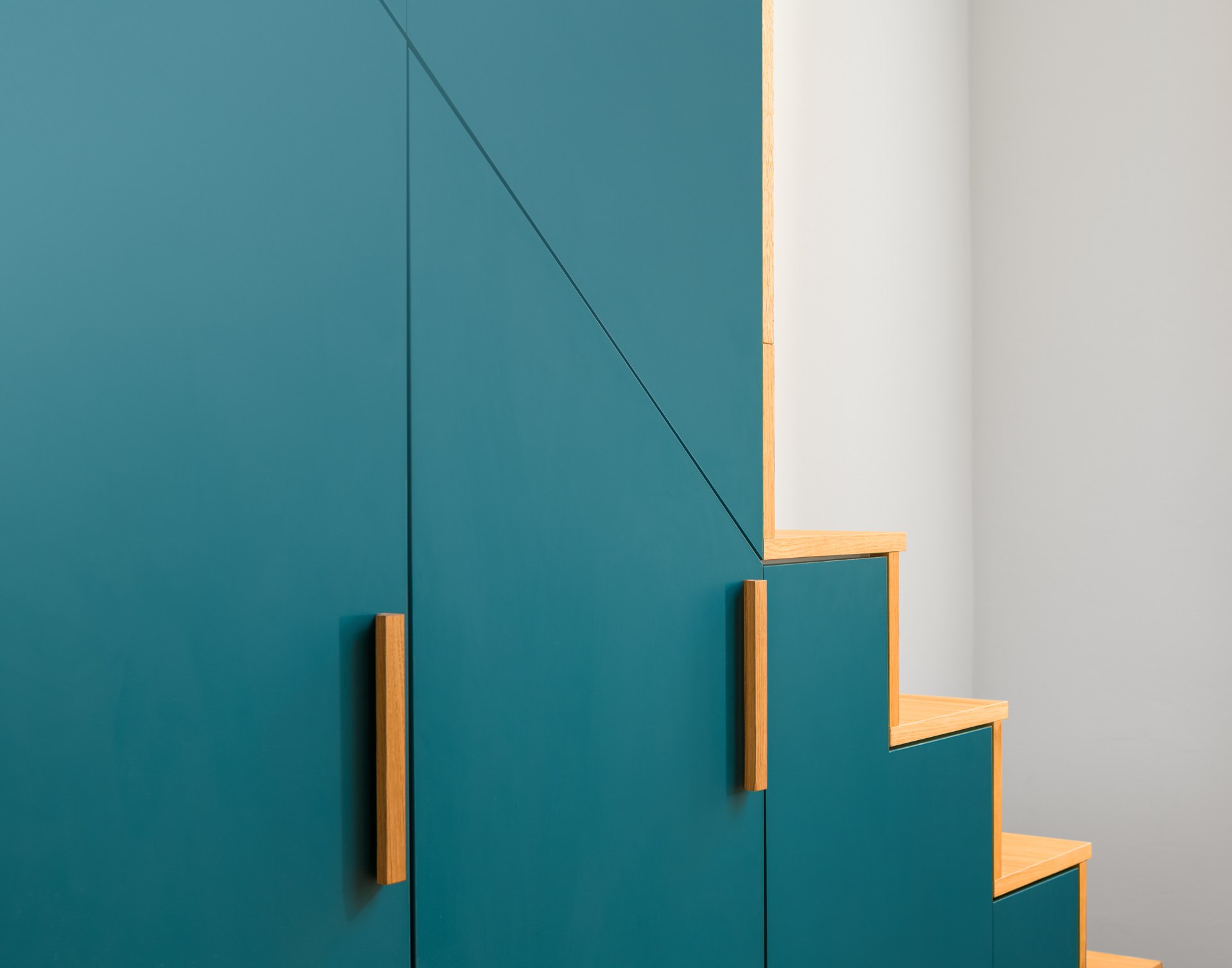 Bold teal fitted wardrobe with geometric stepped upper edge and a brass handle — architectural interior design photography
