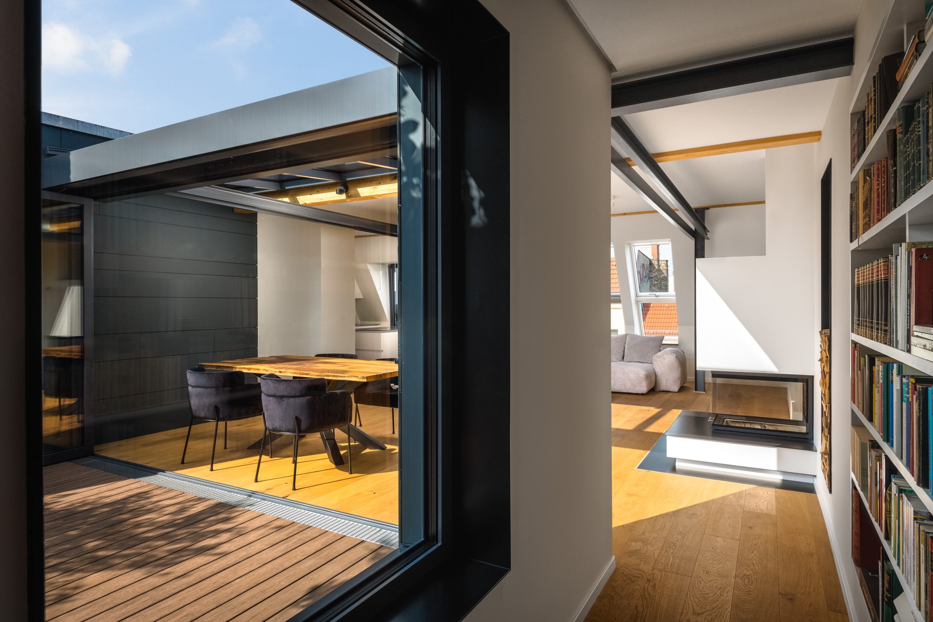 Framed architectural perspective from a terrace into a loft interior with built-in bookshelves and a workspace