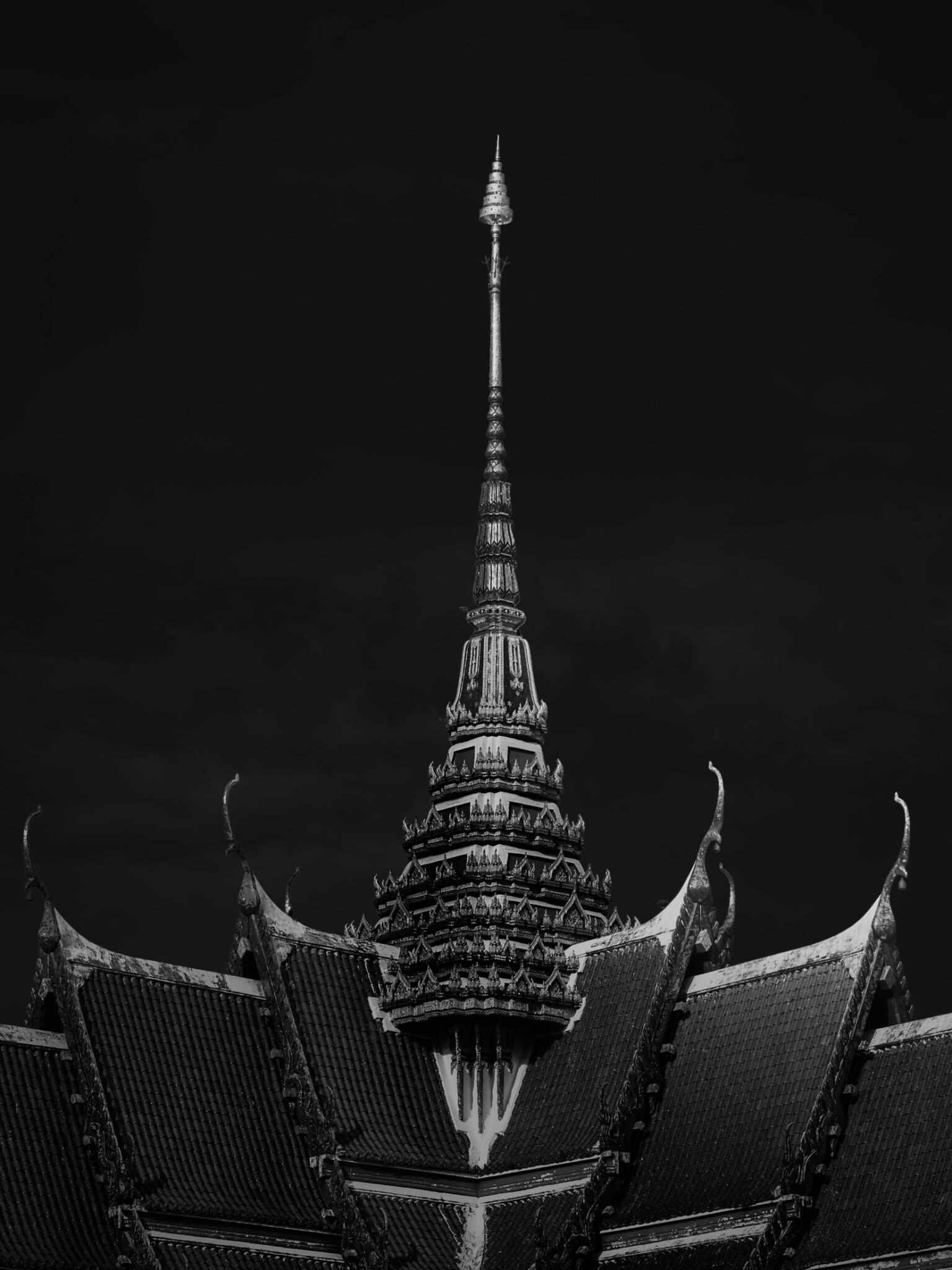 Black and white fine art photograph looking up at an ornate Thai temple spire with layered decorative rooftops