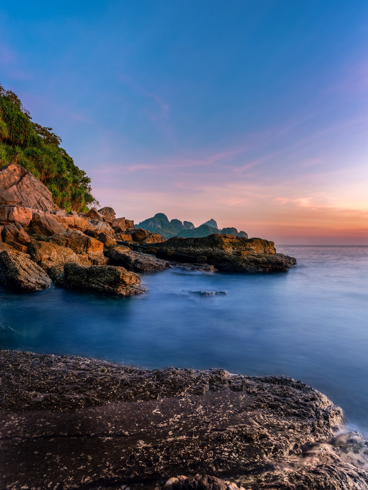 Rocky coastline at golden hour with warm pink and orange sunset sky reflecting on calm ocean water