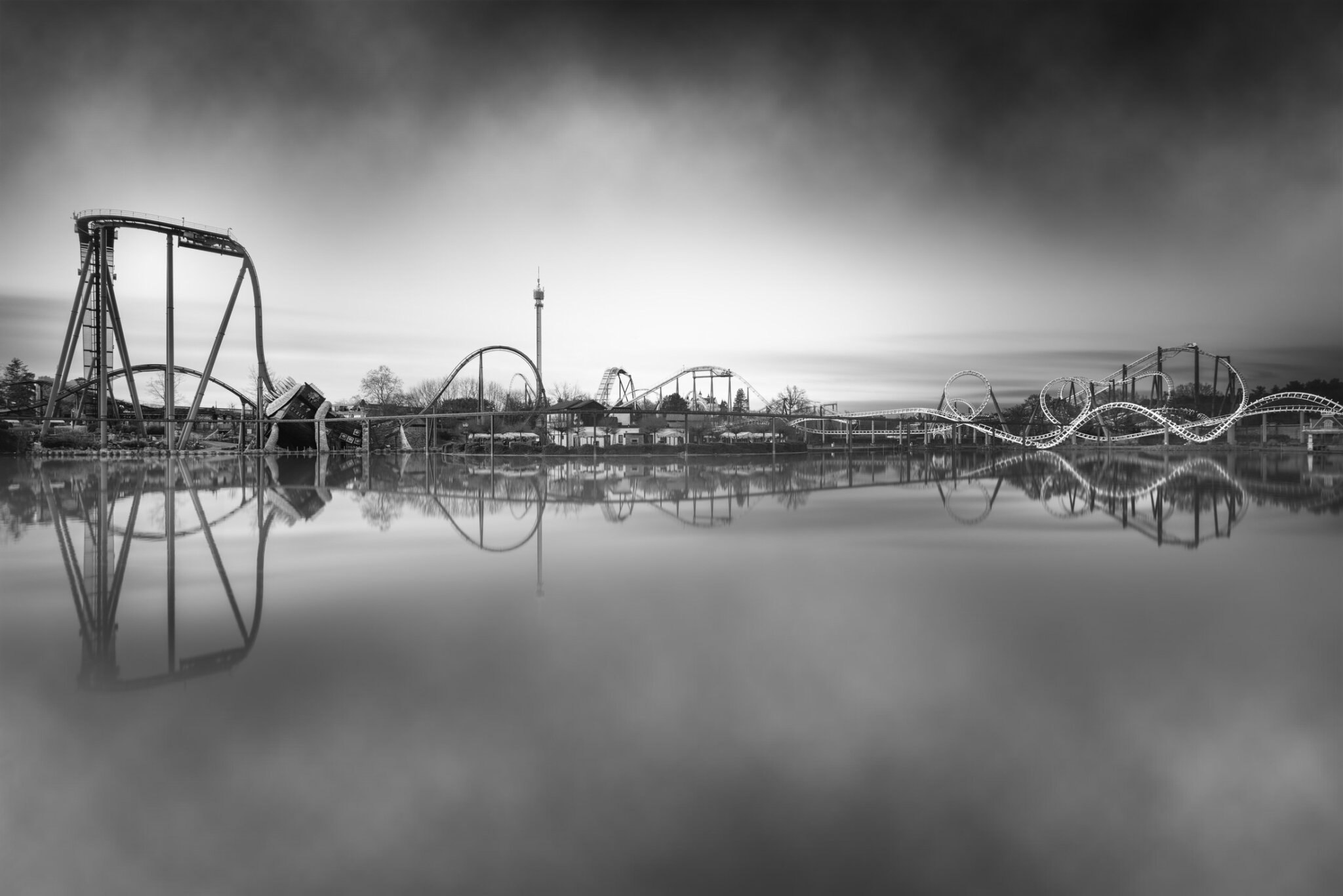 Long exposure black and white fine art photograph of a full theme park skyline reflected in a calm lake at dusk
