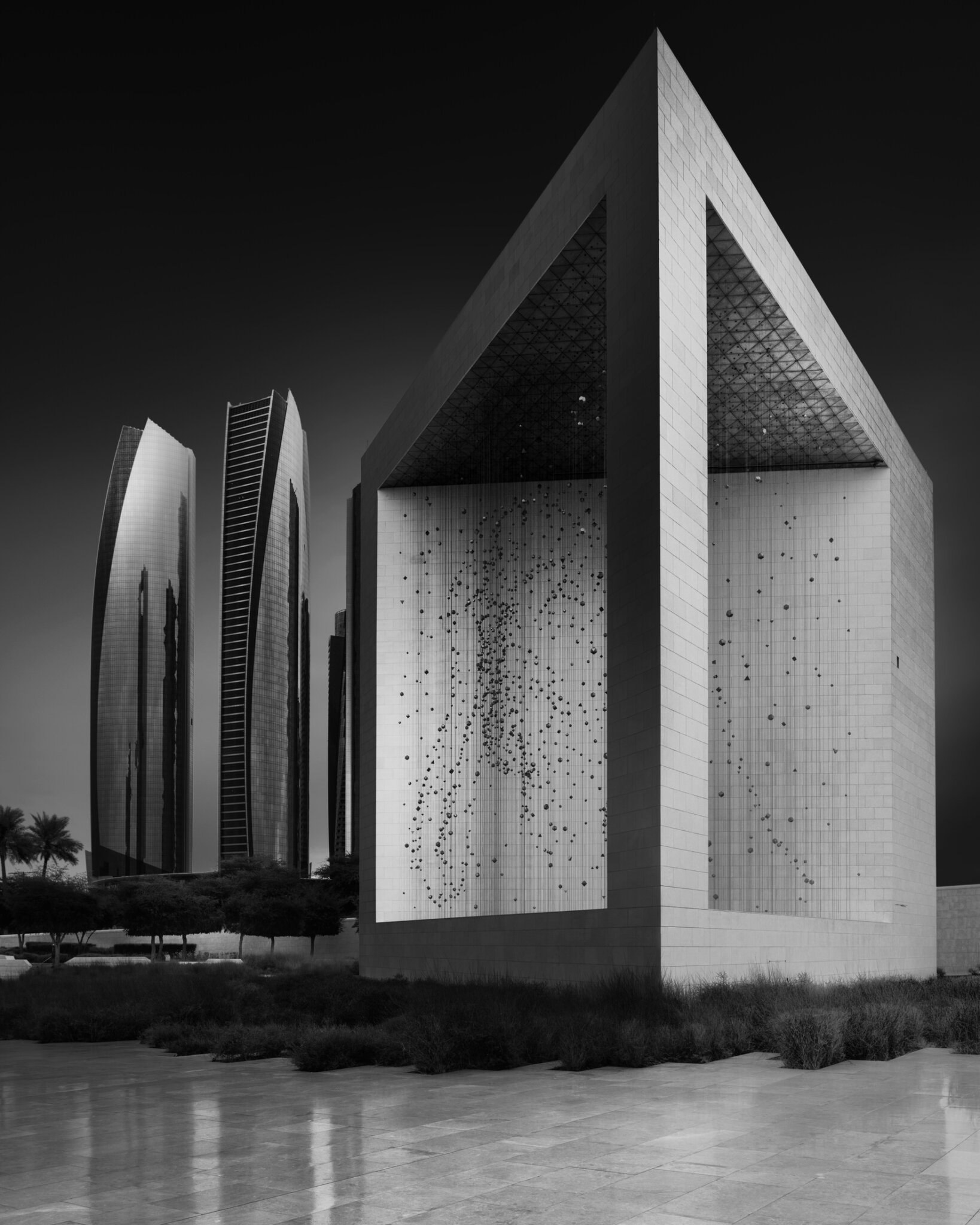 Black and white fine art photograph of a monumental triangular memorial structure illuminated at night with water reflections
